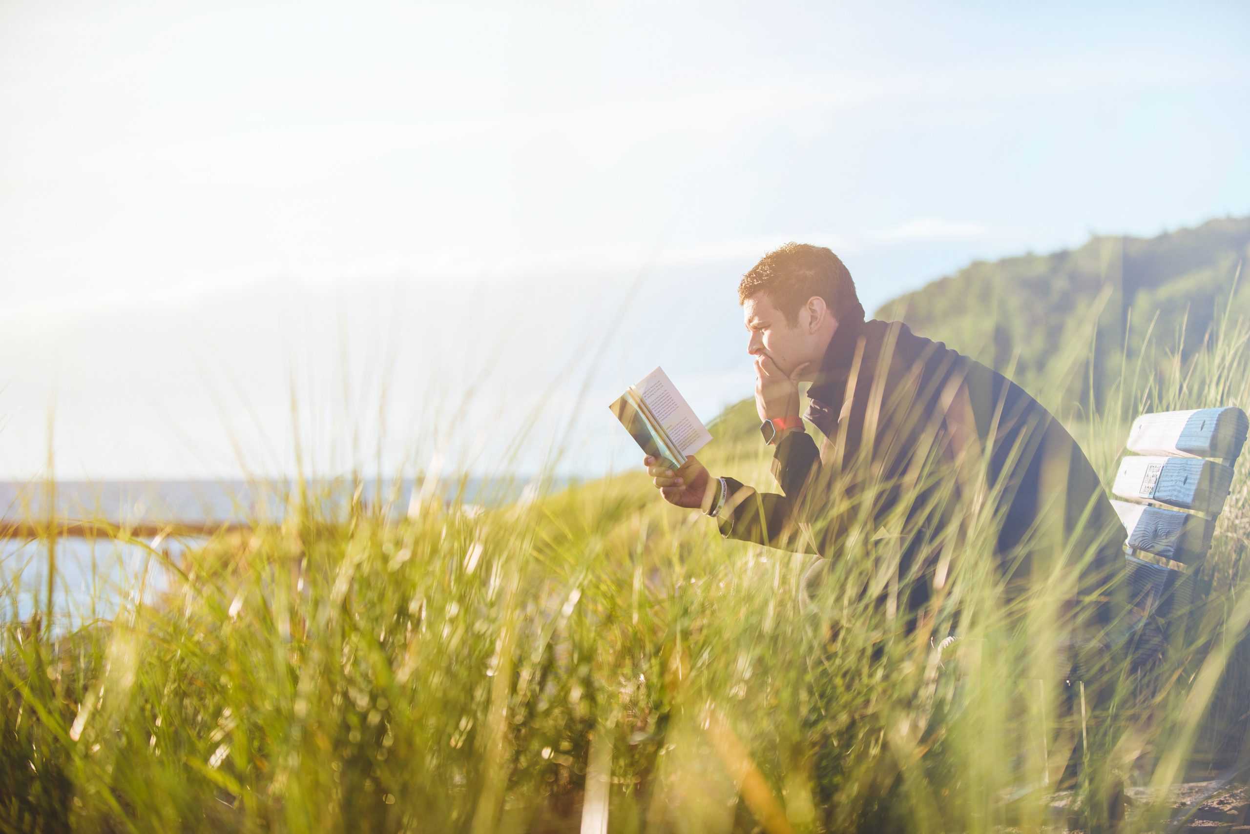 En mann sitter på en benk og leser en bok