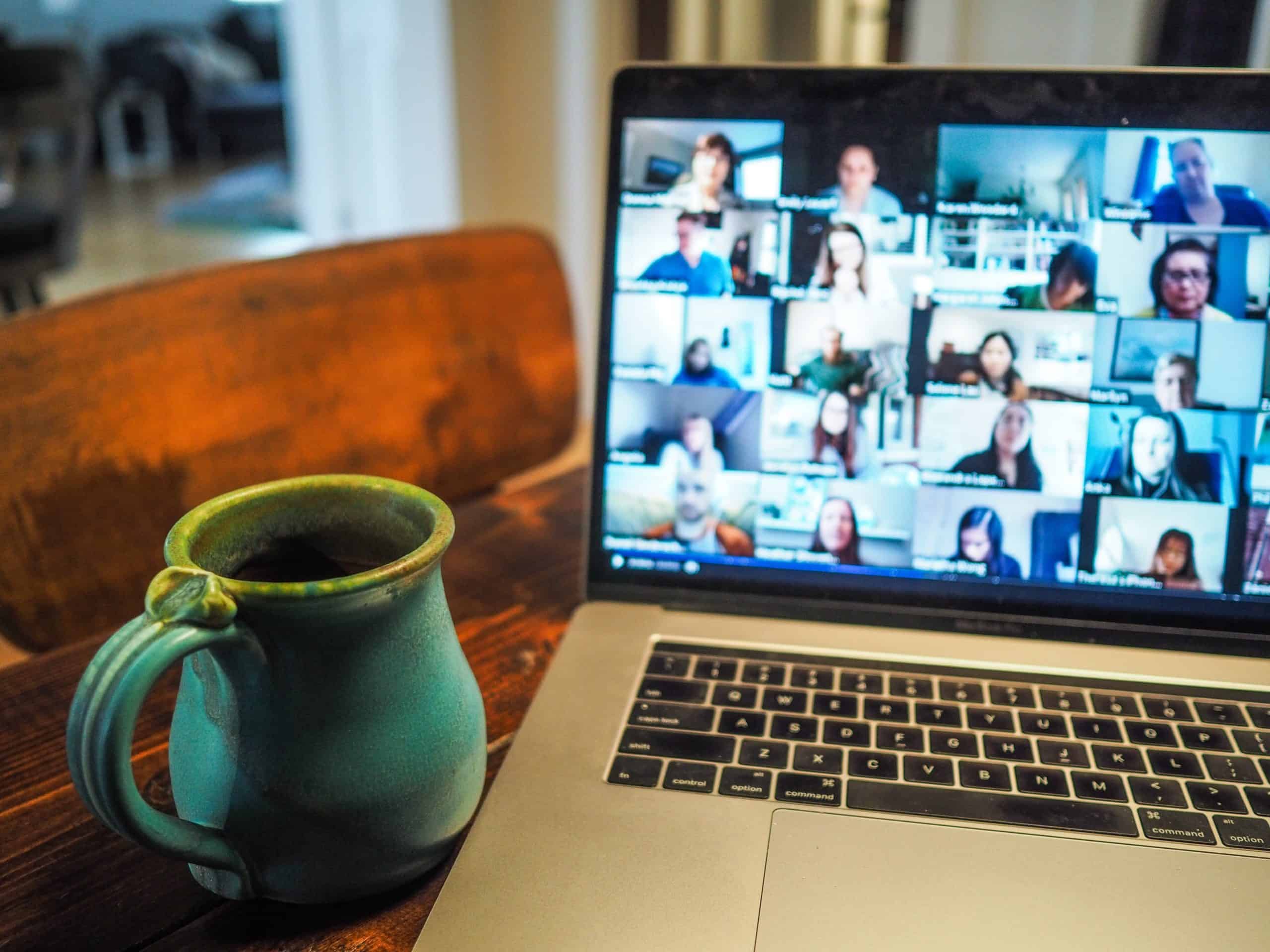 En kaffekopp, og en PC som viser at personen snakker med flere personer på et teams-møte