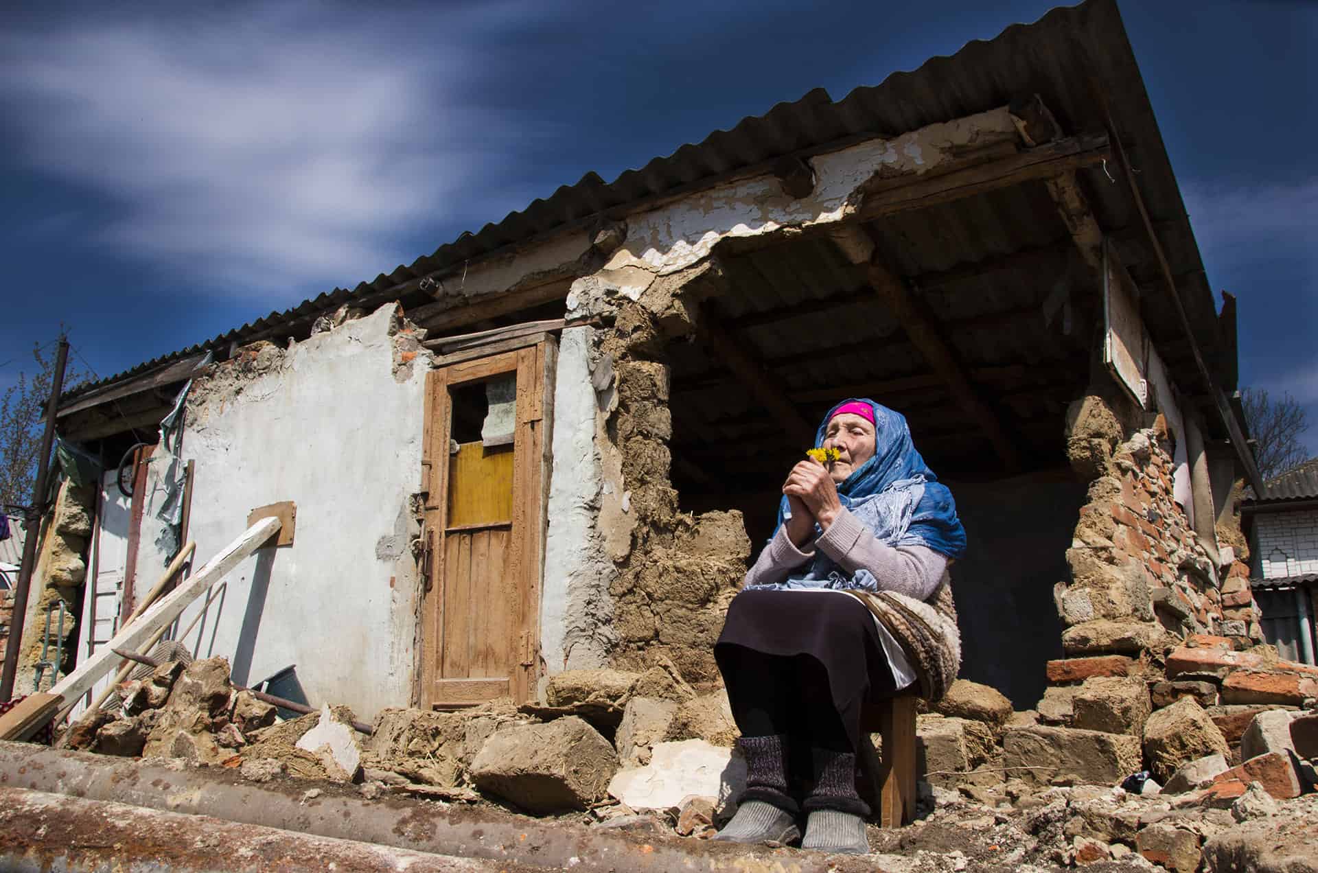 En eldre kvinne i Ukraina sittende ved et hus ødelagt av krigen