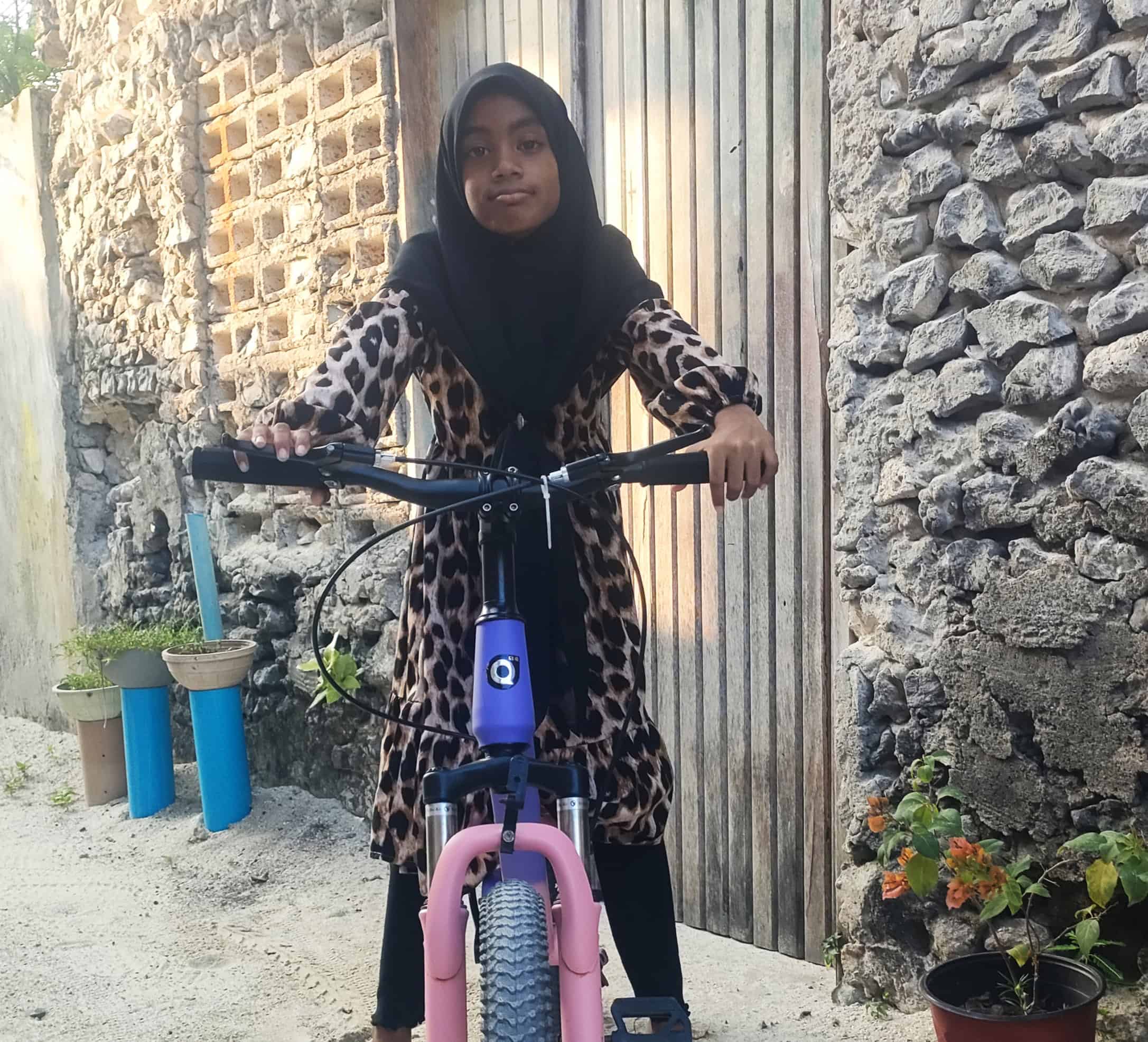 Ti år gamle Rihanna fra Maldivene poserer på en lilla sykkel utenfor et steinhus. Ti år gamle Rihanna fra Maldivene poserer på en lilla sykkel utenfor et steinhus.