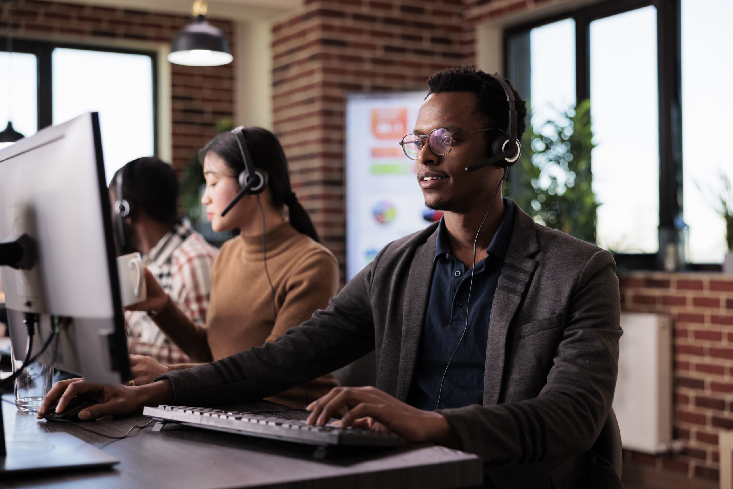 African american helpline employee working at call center reception with multiple monitors. Male operator using telecommunication to help clients at customer service support, remote network. African american helpline employee working at call center reception with multiple monitors. Male operator using telecommunication to help clients at customer service support, remote network.