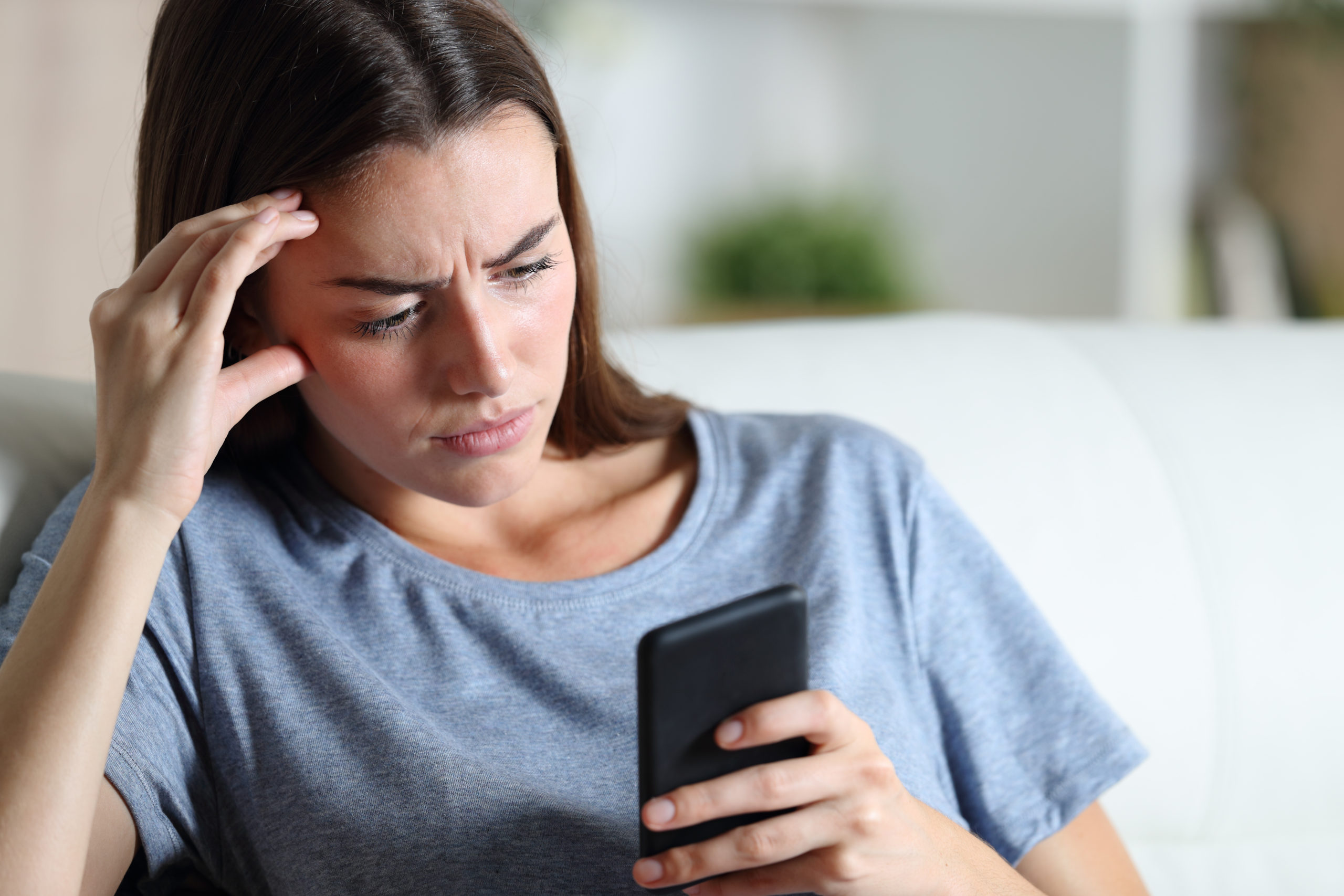 Worried,Girl,Checking,Smart,Phone,Sitting,On,A,Couch,In